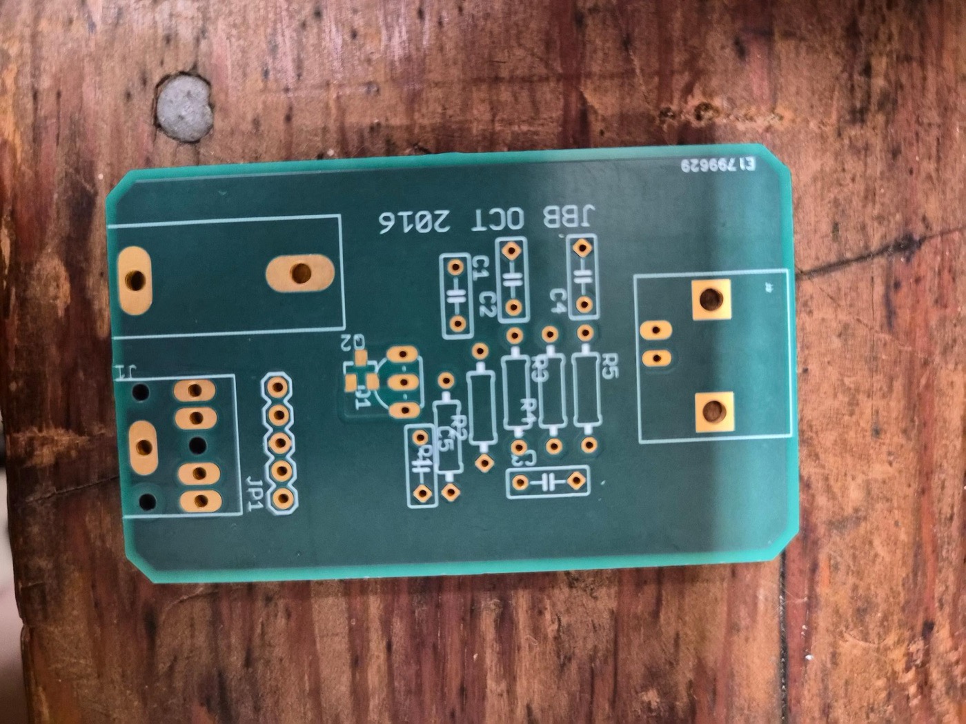 A bare green printed circuit board for a small JFET preamplifier, lying on a wooden bench.