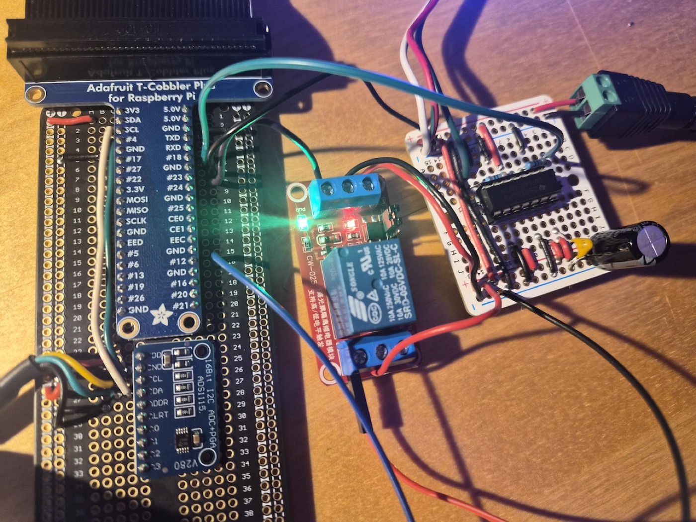A breadboard with a Raspberry Pi cobbler, a 16-bit ADS1115 analog-to-digital converter, a relay module, and a hand-soldered perfboard circuit.